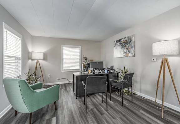 A room with a green chair and a desk with a laptop and other items on it.