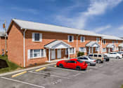 Thumbnail 13 of 13 - A red car is parked in a parking lot in front of a brick building.