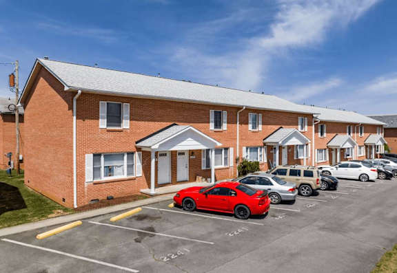 A red car is parked in a parking lot in front of a brick building.