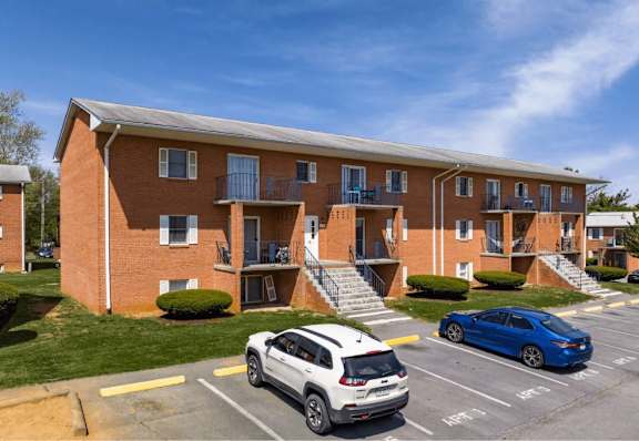 A white car is parked in a parking lot in front of a red brick apartment building.