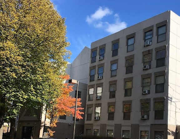 A tall building with many windows is surrounded by trees.