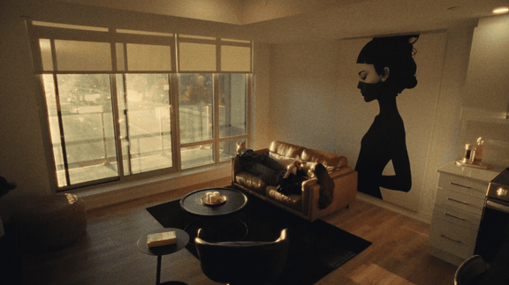 A woman in a black dress stands in a living room with a couch and a coffee table.