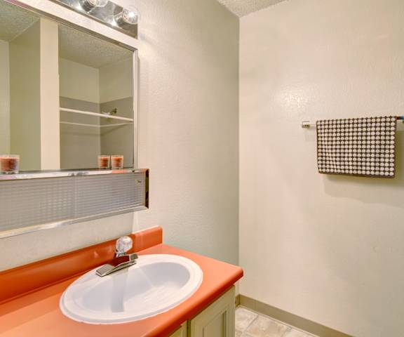 The bathroom with a shower, sink with an orange counter, and mirror at Quiet Creek Apartment Homes. 