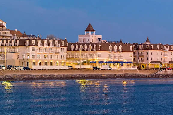 A large white building with a tower sits on the shore of a body of water.