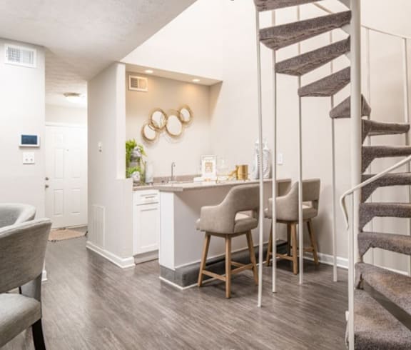 a living room with a spiral staircase and a kitchen with a bar and chairs