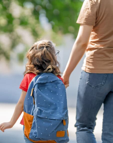 A child with a blue backpack is walking with an adult.