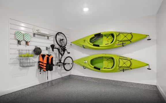 A room with two kayaks hanging on the wall and a bicycle hanging from the wall.