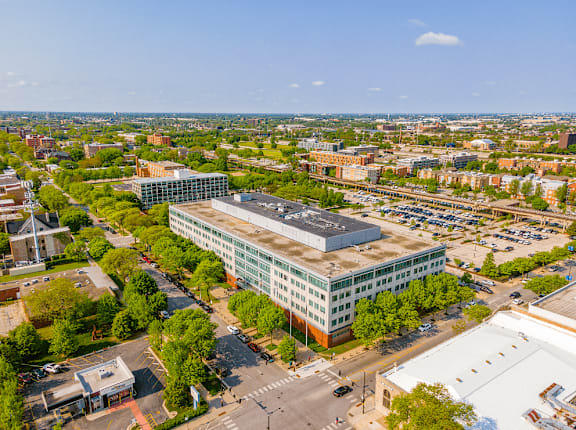 A large building with a glass facade is surrounded by trees and other buildings.