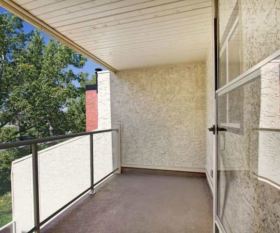 A balcony with a white wall and a door and a tree at 3600 Brentwood. 