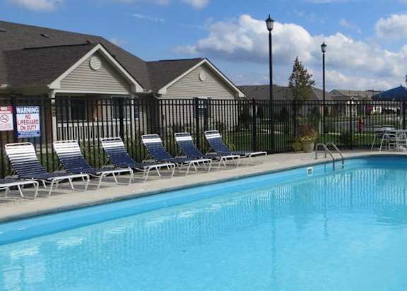 A swimming pool surrounded by a black fence and lounge chairs.