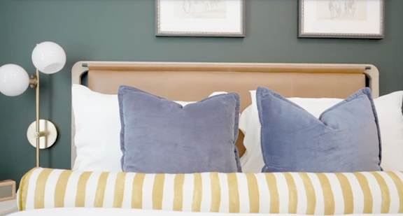 A bed with a yellow and white striped pillowcase and two blue cushions.