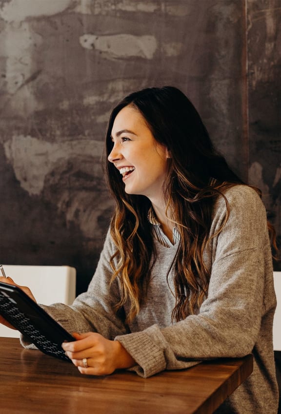 a woman sitting at a desk laughing while using a laptop computer