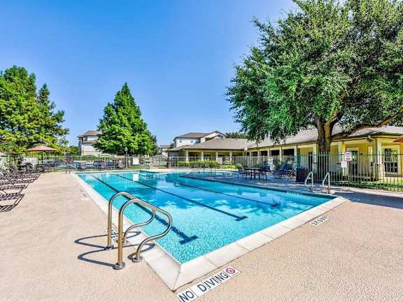 A swimming pool surrounded by trees and a building in the background.