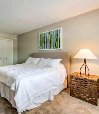 A bedroom with a large bed and a wooden nightstand.