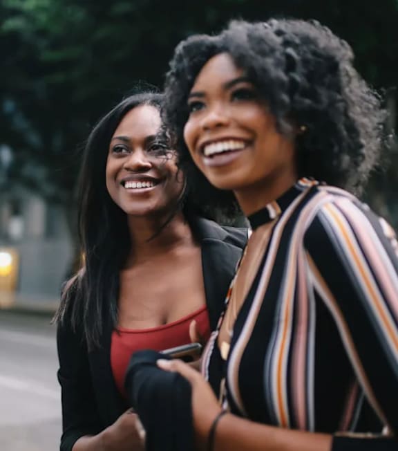 Two women laughing together on a city street.at Sutton Collection, New York, NY