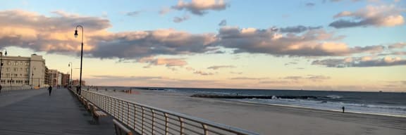 A wooden boardwalk with a metal railing runs parallel to a sandy beach.