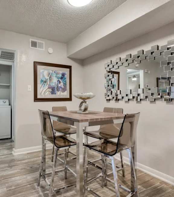 A laundry room with a washer and dryer, a dining table with chairs, and a mirror with a frame.