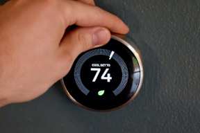 A person is adjusting a thermostat set to 74 degrees.