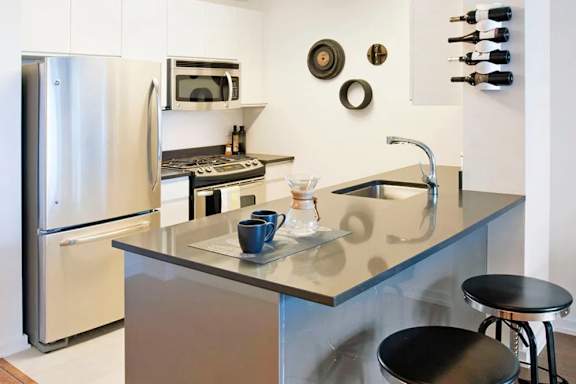 A kitchen with a refrigerator, microwave, and a sink at The Maximilian Apartments, Long Island City, NY