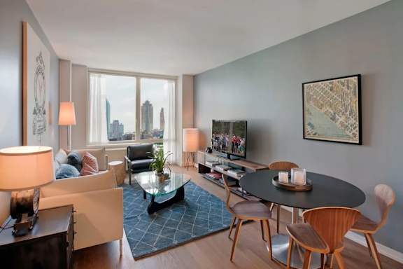 A living room with a view of the city skyline through the windows at The Maximilian Apartments, Long Island City, 11101