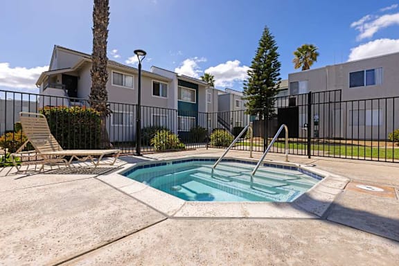 A pool surrounded by a black fence with a chair and a tree in the background.