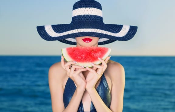 a woman wearing a hat and holding a slice of watermelon in front of her face at Regatta at New River, Fort Lauderdale, FL