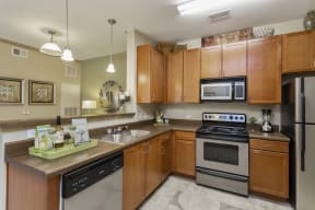 The Grove at Waterford Crossing Kitchen with Black/Stainless Steel Appliances, Wood Cabinets, and Access to Living Room