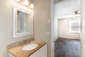 Murfreesboro Apartments for Rent - Condos at the Villager - Bathroom With Sleek Counters, a Mirror With a Row of Lights, and Access to the Bedroom