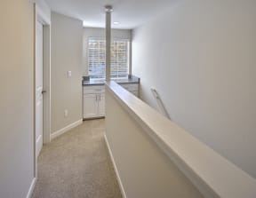 Upstairs carpeted hallway, banister to the right with large window at the top of stairs with counter and cabinets.