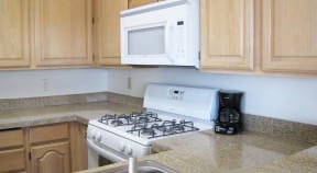 Kitchen with upper and lower cabinets, and white microwave and oven with stove cooktop.