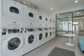 a spacious laundry room with white washers and dryers and a white table with a blue