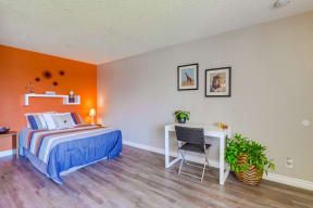 Las Brisas Apartments in Colton - Bedroom with Stylish Decor, Plank Flooring, Beige and Orange Walls, Small Shelf, and Popcorn Ceiling