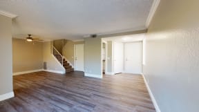 Apartments in Ontario CA - Rancho Vista - Unfurnished Living Room With Wood Styled Flooring, a View of the Dining Room, and Adjacent Entryway and Guest Bathroom