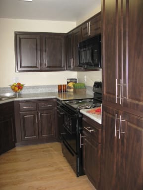 Apartments for Rent in Antelope Valley, CA - The Arches at Regional Center West Kitchen with Black Appliances, Granite Countertops, Plank Flooring, and Dark Mocha Cabinets