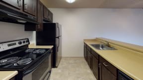 Ontario CA Apartments - Encore Apartment Homes - Kitchen with Dark Wood-Style Cabinets, Plenty of Counterspace, Tile Flooring, and Black & Stainless Steel Appliances