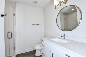 renovated home | bathroom with white cabinets, round mirror, shower stall
