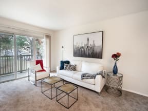 a living room with a white couch and chairs and a sliding glass door leading to a balcony