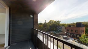 Private balcony with metal railing overlooking street and brick building across from it