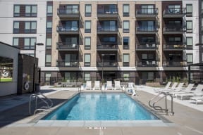 Outdoor pool at Arcata Apartments with white lounge chairs around it.