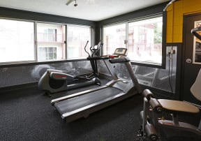 24 hour fitness center with a treadmill and elliptical lit by two large windows.