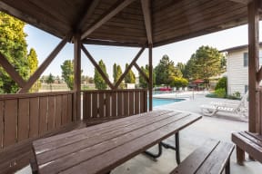 Shaded community gazebo with picnic table, seating, and a view looking out to the pool.