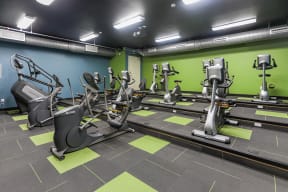Workout space in the cardio theater equipped with a variety of cardio and strength equipment facing a large TV screen.