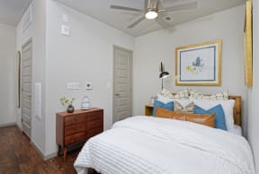 Furnished bedroom with white sheets on bed, small dresser and ceiling fan