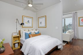 Furnished bedroom with white sheets, nightstand and ceiling fan, opens to living room