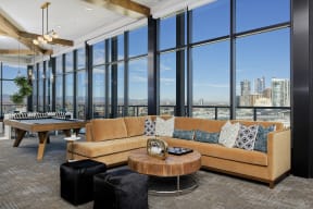Sky lounge with sectional couch, pool table and large glass windows with view of Denver skyline