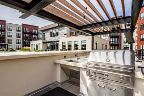 Outdoor grilling station with counterspace and a sink all shaded by an overhead pergola.