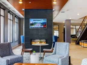 Lobby area with blue lounge chairs, floor to ceiling fireplace with mounted TV above