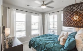 Furnished bedroom with twin bed, dark wood dresser and windows for natural light