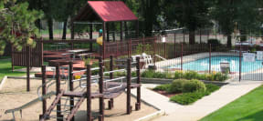 outdoor children's play structure next to grilling pavilion and gated outdoor pool