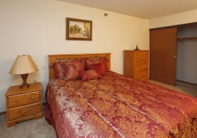 Furnished bedroom with red patterend bedspread, side table and dresser
